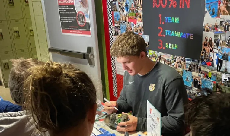 DCY Swim Alum Max McHugh signs autographs at a table surrounded by Jingle Bell swim meet participants